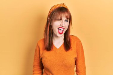 Kızıl saçlı, turuncu süveter giyen genç bir kadın kameraya seksi bir ifadeyle bakıyor, neşeli ve mutlu bir yüzle.. 