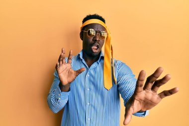 Kafasına kravat takan yakışıklı, sarhoş, güneş gözlüklü, korkmuş ve korkudan dehşete düşmüş bir zenci. El hareketlerini durdur, şok içinde bağır. panik konsepti. 