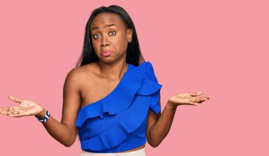 Sıradan kıyafetler giyen, elleri ve kolları havada, kafası karışmış genç siyahi bir kadın. şüphe kavramı. 