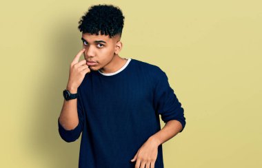 Gündelik giysiler giymiş genç Afro-Amerikan bir adam senin jestini izlerken, şüpheli bir ifade takınıyor. 