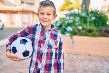 Parkta futbol topunu tutarken mutlu gülümseyen sevimli beyaz çocuk..