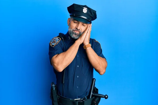 Middle age handsome man wearing police uniform sleeping tired dreaming and posing with hands together while smiling with closed eyes.