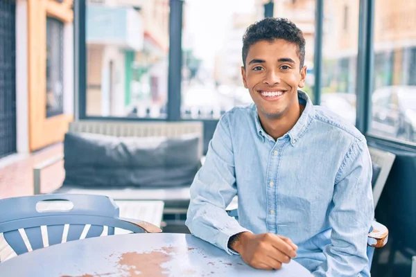 Young latin man smiling happy sitting at coffee shop terrace.