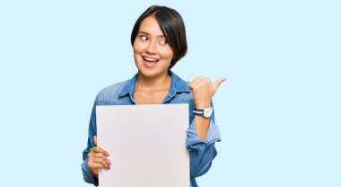 Kısa saçlı güzel bir kadın boş bir pankart tutuyor başparmağıyla yan tarafa bakıyor ve ağzı açık gülümsüyor. 