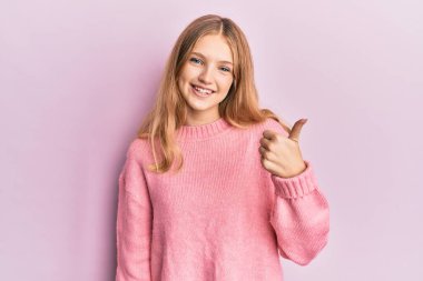 Güzel, genç, beyaz bir kız günlük kıyafetler giyip el hareketleriyle mutlu mesut bir jest yapıyor. Kameraya bakıp başarıyı gösteren ifade. 