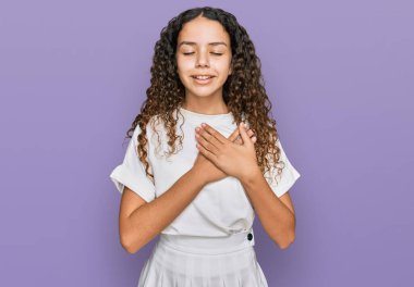 Gündelik beyaz tişört giyen genç İspanyol kız elleri göğsünde, gözleri kapalı gülümsüyor ve yüzünde minnet ifadesi var. sağlık kavramı. 