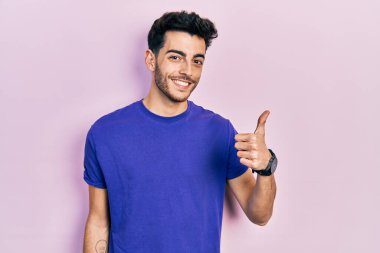 Gündelik tişört giyen İspanyol genç adam elleriyle mutlu bir jest yapıyor. Kameraya bakıp başarıyı gösteren ifade. 