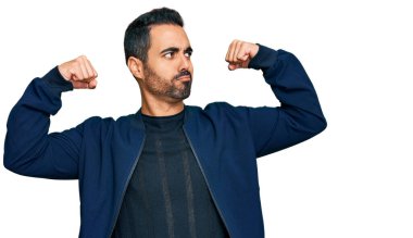 Sıradan kıyafetler giyen genç İspanyol adam gururla gülümseyen kol kaslarını gösteriyor. fitness konsepti. 