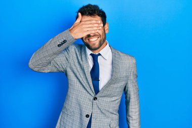 Sakallı, takım elbiseli, kravatlı, gülümseyen ve yüzünü kapatan yakışıklı bir adam. kör kavram. 