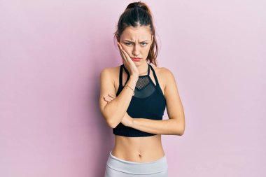 Spor giyinen genç esmer kadın kollarını kavuşturarak depresyondan sıkılmış ve yorgun görünüyor.. 