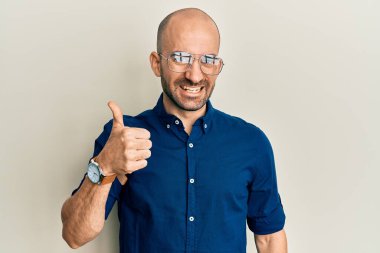 Gündelik kıyafetler ve gözlük takan genç İspanyol adam mutlu ve pozitif gülümsüyor, başparmağıyla mükemmel ve onay işareti yapıyor. 