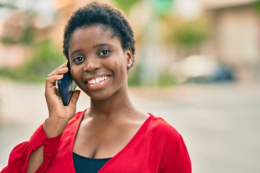 Genç Afrikalı Amerikalı kadın gülümsüyor. Şehirdeki akıllı telefondan mutlu bir şekilde konuşuyor..