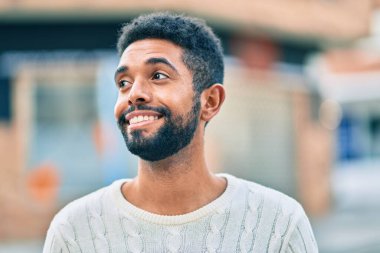 Genç Afrikalı Amerikalı adam gülümseyerek şehirde mutlu mesut duruyor..