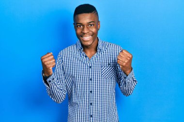 Gündelik giysiler giyen genç Afro-Amerikalı adam kollarını kaldırıp, gözleri açık bir şekilde başarıyı kutluyor ve şaşırıyor. Kazanan konsept. 
