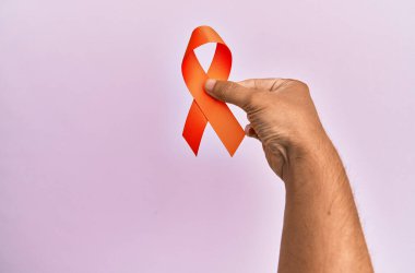 İzole edilmiş pembe arka planda turuncu kurdele tutan İspanyol bir adamın eli..