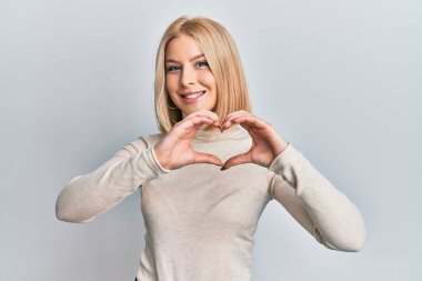 Sıradan kıyafetler giyen, aşık gülümseyen, elleriyle kalp sembolü yapan genç sarışın kadın. romantik kavram. 