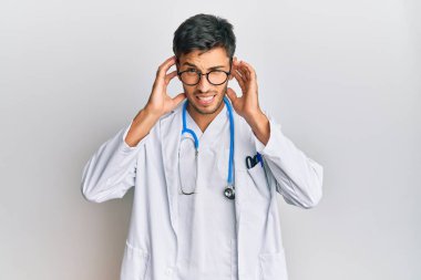 Doktor üniforması giyen genç yakışıklı bir adam ve yüksek sesli müzik sesi için kulakları parmaklarıyla kapatan steteskop. sağır kavramı. 