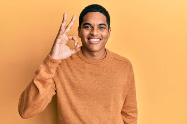 Kış süveteri giyen genç, yakışıklı İspanyol adam gülümsüyor ve el ve parmaklarıyla 