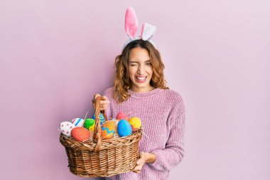 Paskalya tavşanı kulaklı, elinde renkli bir yumurta olan beyaz bir kadın kameraya seksi bir ifadeyle bakıyor, neşeli ve mutlu bir yüz.. 