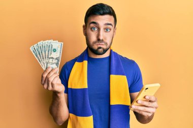 Genç İspanyol futbolcu destekçisi Amerikan dolarlarını elinde tutarak komik yüzlü yanakları şişiren akıllı telefon kullanıyor. Ağzı havayla şişer, havayı yakalar.. 