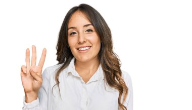 Genç esmer kadın gündelik giysiler giyip üç numaralı parmaklarıyla işaret ederken kendinden emin ve mutlu bir şekilde gülümsüyor.. 