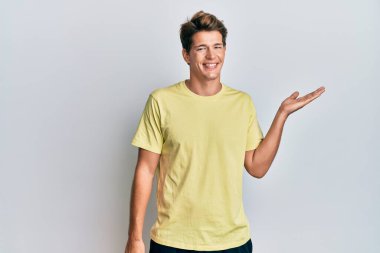 Yakışıklı, günlük kıyafetler giyen, neşeli bir şekilde gülümseyen, avuç içiyle kameraya bakan beyaz bir adam.. 