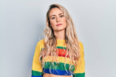 Renkli süveter giyen güzel sarışın kadın yüzünde ciddi bir ifadeyle rahatlamış. Basit ve doğal bir şekilde kameraya bakıyorsun.. 