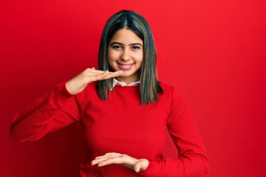 Elleriyle el kol hareketi yapan gündelik kıyafetler giyen genç Latin kadın büyük ve büyük beden işareti, ölçü sembolü gösteriyor. Kameraya bakıp gülümsüyor. ölçüm kavramı. 