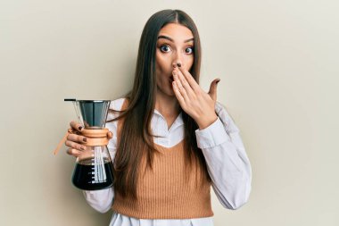 Güzel esmer kadın, elinde çözünebilir kahve makinesiyle ağzını eliyle kapatıyor. Şok olmuş ve hata yapmaktan korkuyor. şaşırmış ifade 