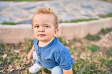 Sevimli ve mutlu küçük çocuk güneşli bir günde parkta eğleniyor. Güzel sarı saçlı erkek çocuk dışarıda oynuyor.