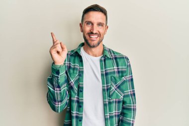 Sakallı, sıradan kıyafetler giyen, yüzünde kocaman bir gülümseme olan, eli ve parmağı kameraya bakan yakışıklı bir adam.. 