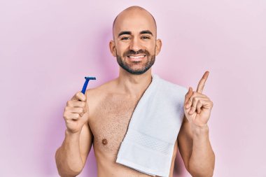 Tıraş bıçağı tutan kel genç adam mutlu bir şekilde elini ve parmağını yana doğru uzattı. 