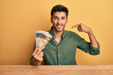 Kanada doları tutan yakışıklı genç bir adam. Kendinden emin görünüyor. Yüzünde gülücükler, parmakları gururlu ve mutlu birini gösteriyor.. 