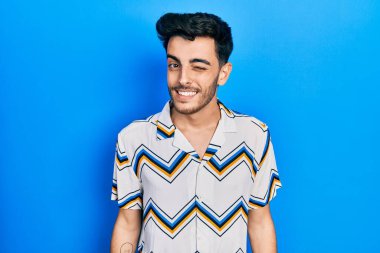 Gündelik kıyafetler giyen genç İspanyol adam kameraya seksi bir ifadeyle bakıyor, neşeli ve mutlu bir yüzle.. 