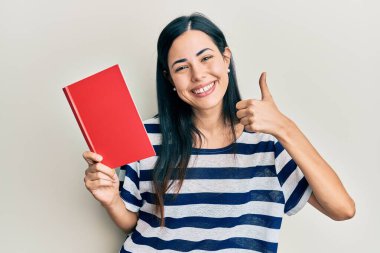 Güzel genç bayan kitap okuyor mutlu ve pozitif gülümsüyor, başparmağıyla mükemmel ve onay işareti yapıyor. 