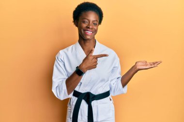 Karate kimonosu ve siyah kuşak giyen genç Afrikalı Amerikalı kız kameraya hayret ediyor ve gülümsüyor.. 