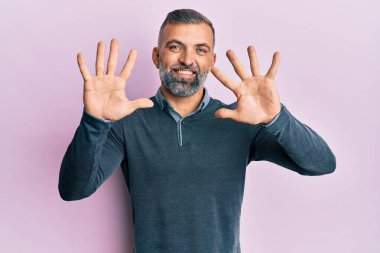 Orta yaşlı, sıradan kıyafetler giyen yakışıklı bir adam on numarayı gösterip işaret ederken kendinden emin ve mutlu bir şekilde gülümsüyor.. 