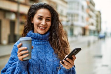 Genç İspanyol kadın akıllı telefon kullanıyor. Şehirde kahve içiyor..