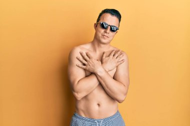 Mayo ve güneş gözlüğü takan yakışıklı genç adam mutlu ve pozitif, kendinden emin gülümsüyor. Sevgi ve özgüven. 