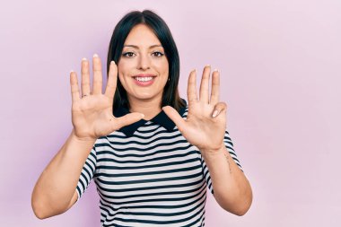 Gündelik kıyafetler giyen genç İspanyol kadın dokuz numarayı gösterip işaret ederken kendinden emin ve mutlu bir şekilde gülümsüyor.. 