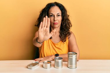Konserve yiyecekleri olan orta yaşlı güzel bir kadın dur işareti yapıyor ciddi ve kendinden emin bir ifadeyle savunma hareketi yapıyor. 