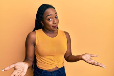 Sıradan kıyafetler giyen, kafası karışmış, elleri ve kolları havada genç bir Afrikalı Amerikalı kadın. şüphe kavramı. 
