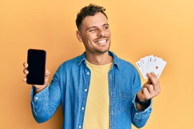 Poker kartları ve akıllı telefon tutan genç İspanyol adam boş ekranı gösteriyor. Gülümsüyor ve başka yöne bakıyor.. 
