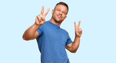 Yakışıklı, sıradan kıyafetler giyen, gülümseyen, parmaklarını zafer işareti yaparken gösteren kaslı adam. İki numara.. 