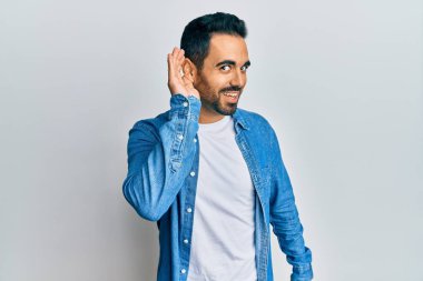 Gündelik kıyafetler giyen, ağzı kulaklarında gülümseyen, dedikoduları ve dedikoduları dinleyen genç İspanyol bir adam. Sağırlık kavramı. 