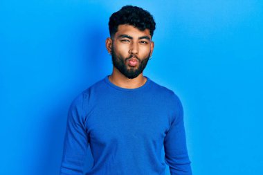 Sakallı, sıradan mavi kazaklı, dudağıyla balık suratı yapan çılgın ve komik bir jest yapan bir Arap. Komik ifade. 