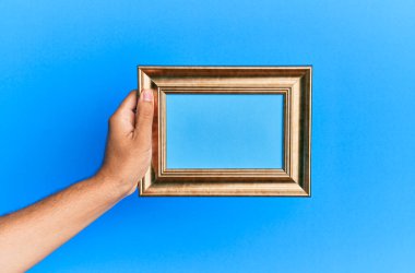 İzole edilmiş mavi arka planda eski bir çerçeveyi tutan İspanyol bir adamın eli..