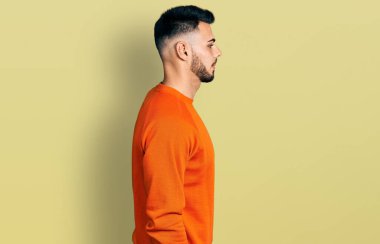 Sakallı, günlük turuncu süveter giyen, rahat bir görünüm takınan, kendine güvenen gülümseyen genç İspanyol bir adam.. 