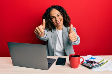 Ofiste çalışan orta yaşlı güzel bir kadın bir fincan kahve içerek olumlu bir jest yapmayı onaylıyor, gülümsüyor ve başarı için seviniyor. kazanan jest. 
