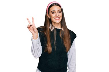 Gündelik beyaz gömlek giyen genç ve güzel bir kadın iki numarayı gösterip işaret ederken kendinden emin ve mutlu bir şekilde gülümsüyor.. 